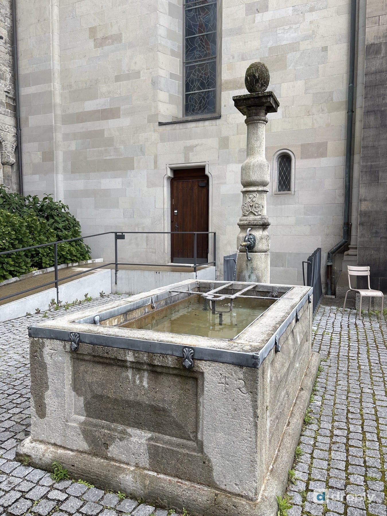 A spring-water fountain with a tree and a tram in the background in Zurich