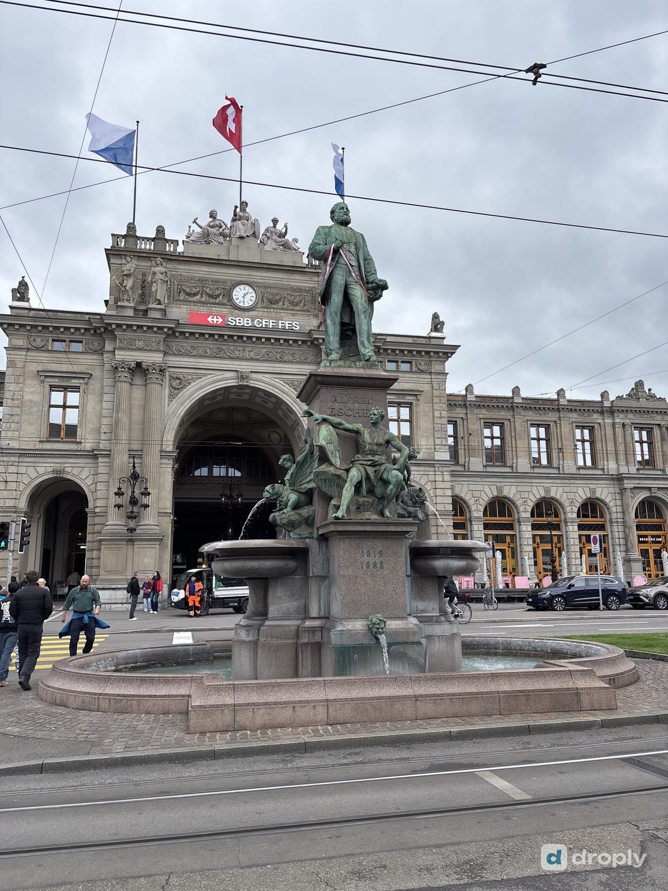 The Alfred Escher fountain in front of Zurich's main train station, with a Swiss flag on Bahnhofplatz