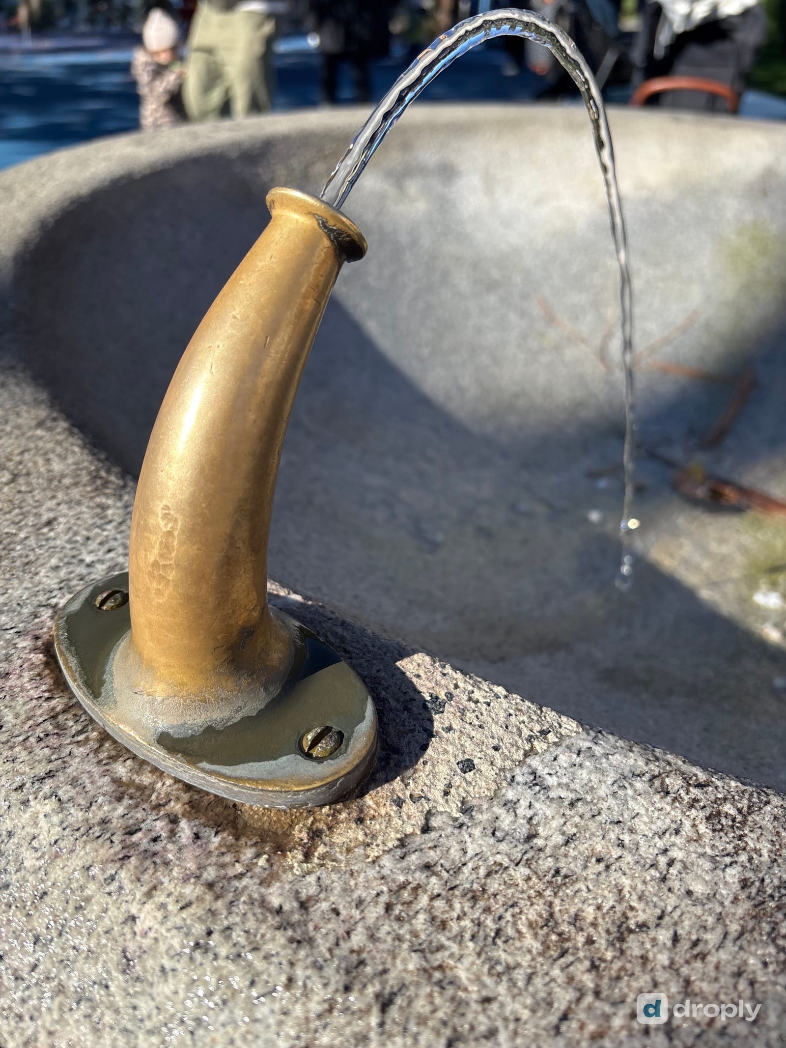 A brass fountain spout set into a granite block, running clear water, in Muralto near Locarno, Ticino