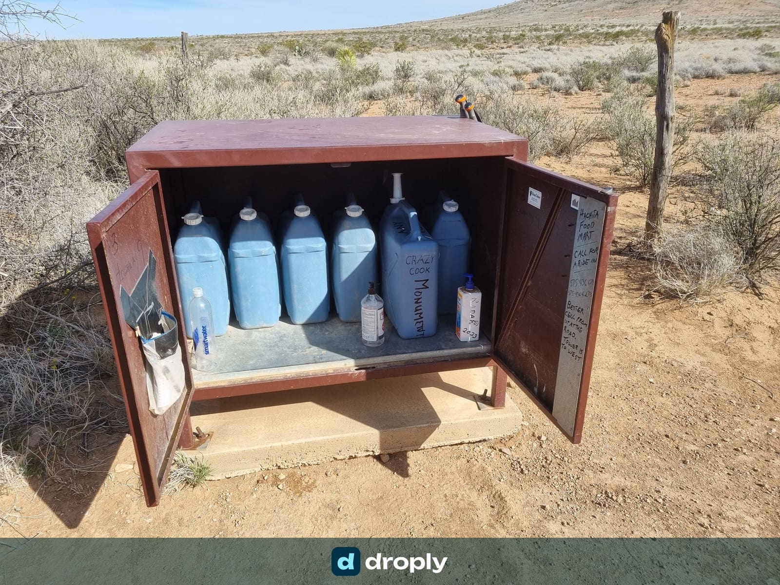 An open metal cache box filled with blue water jugs in the New Mexico desert