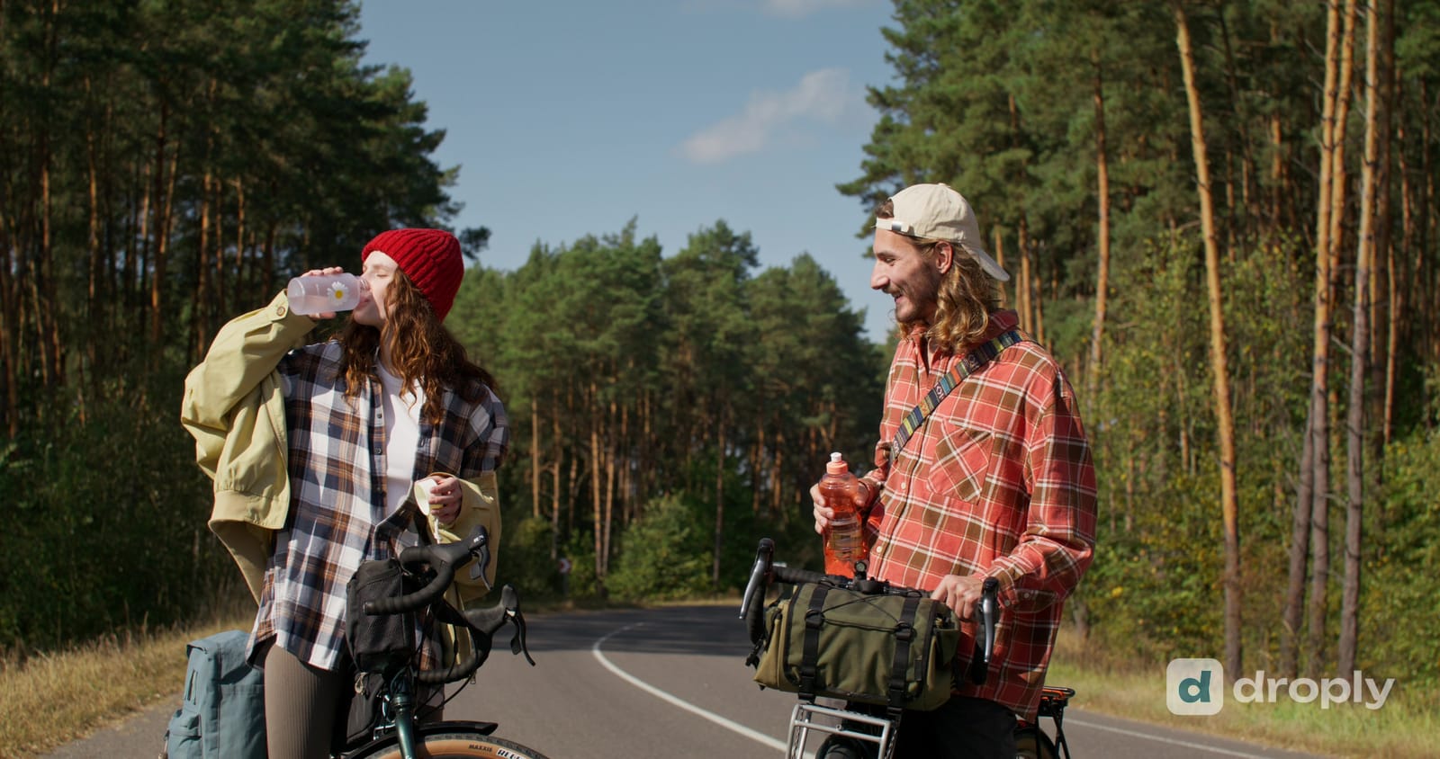 Two cyclists stopped at the side of a forest road, both drinking from bottles
