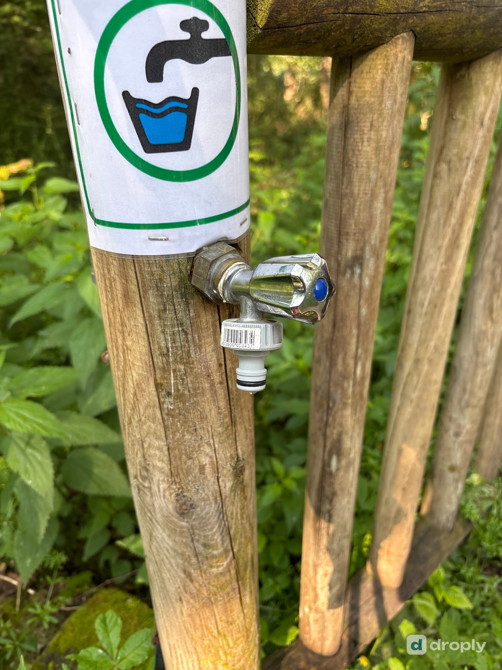 A tap on a wooden post with a green drinking water pictogram, on the trail near Golinhac in Aveyron, France