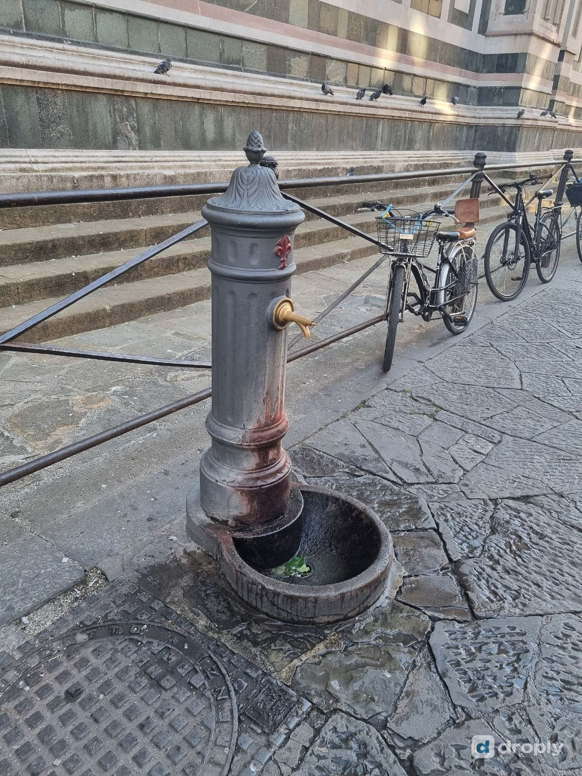 An old iron drinking tap on a Florence street, next to parked bicycles and a stone building