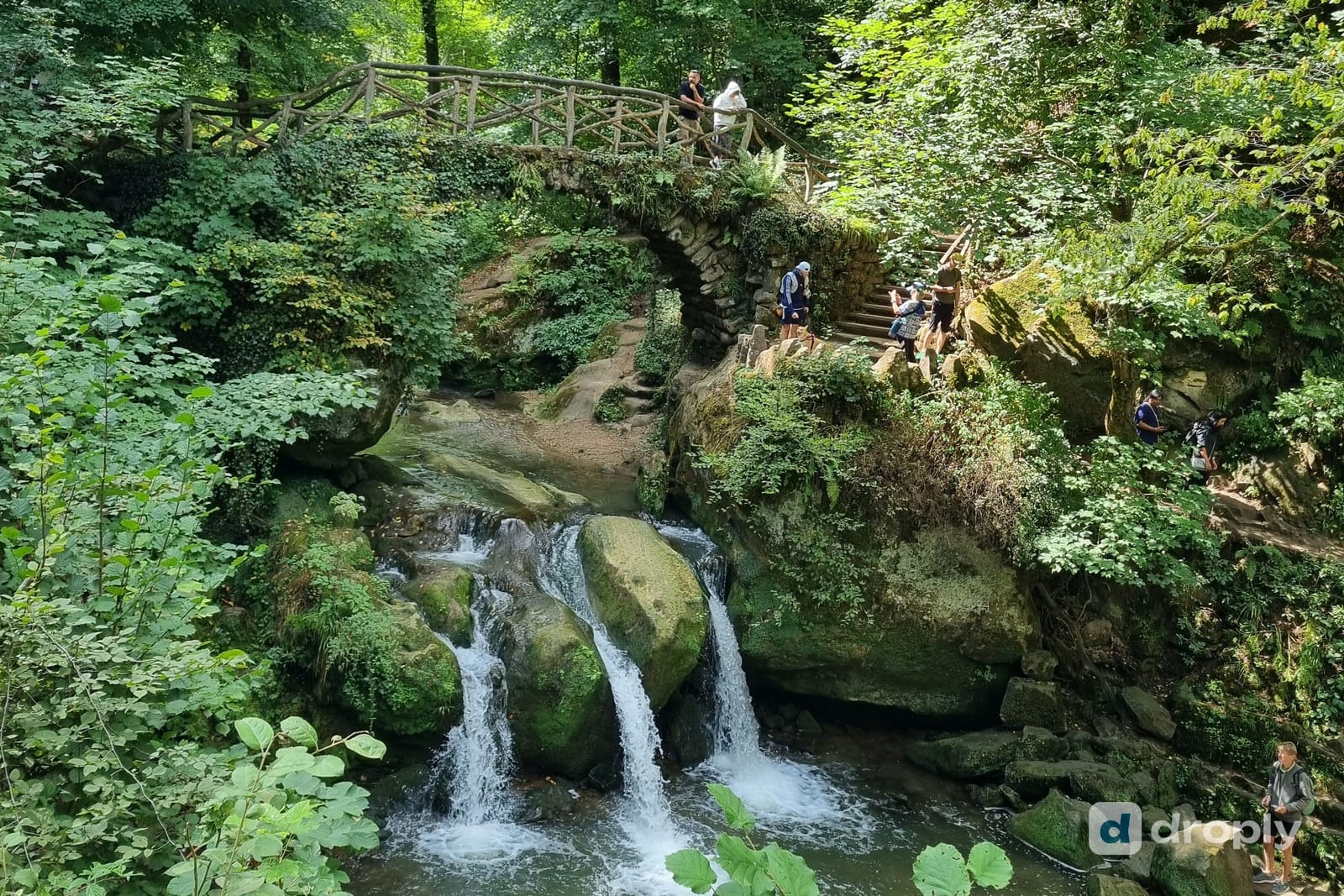 The Schéissendëmpel waterfall with its stone bridge and wooden staircase on the Mullerthal Trail in Luxembourg