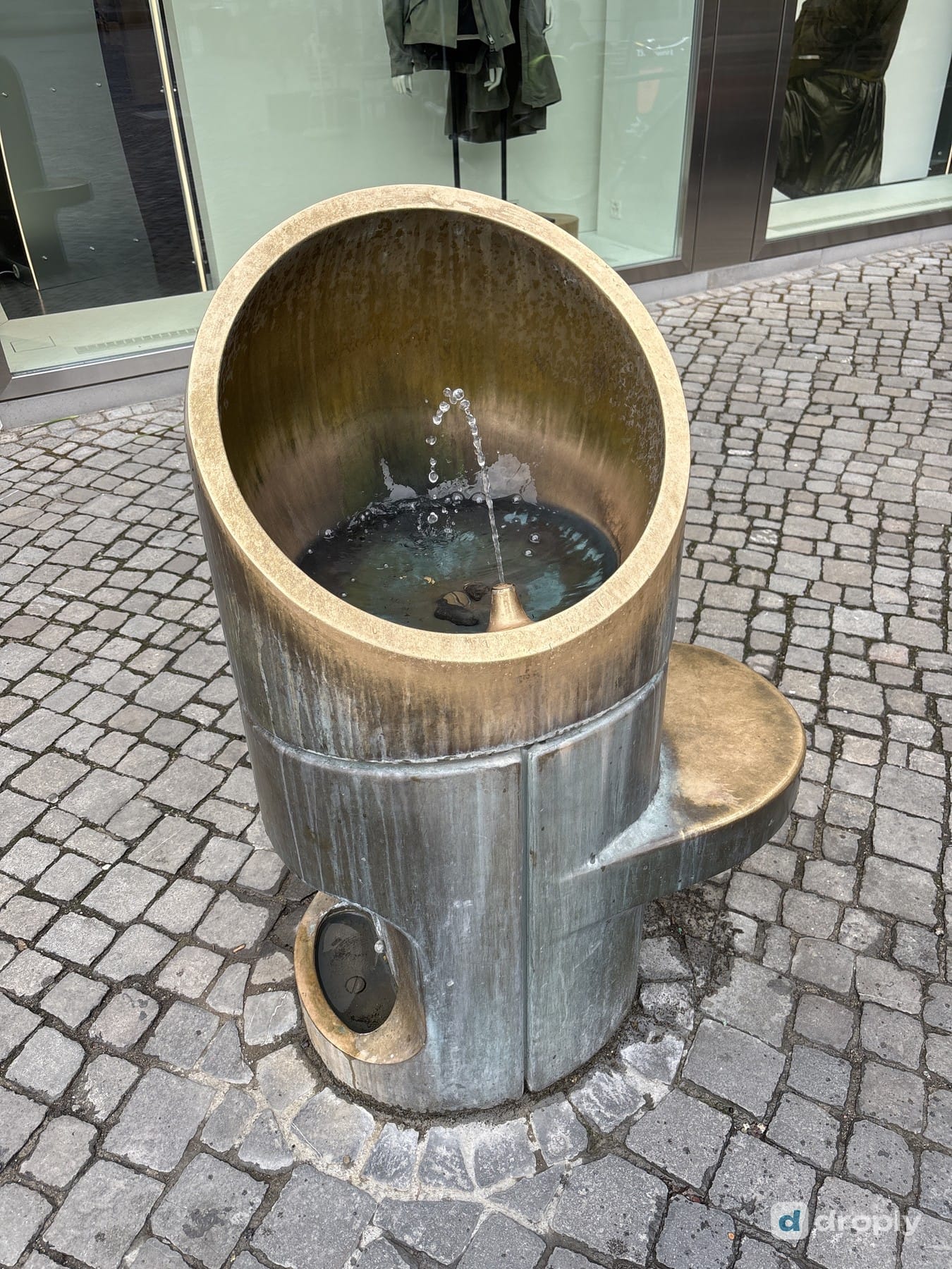 A modern, cylindrical emergency fountain with flowing water in Zurich