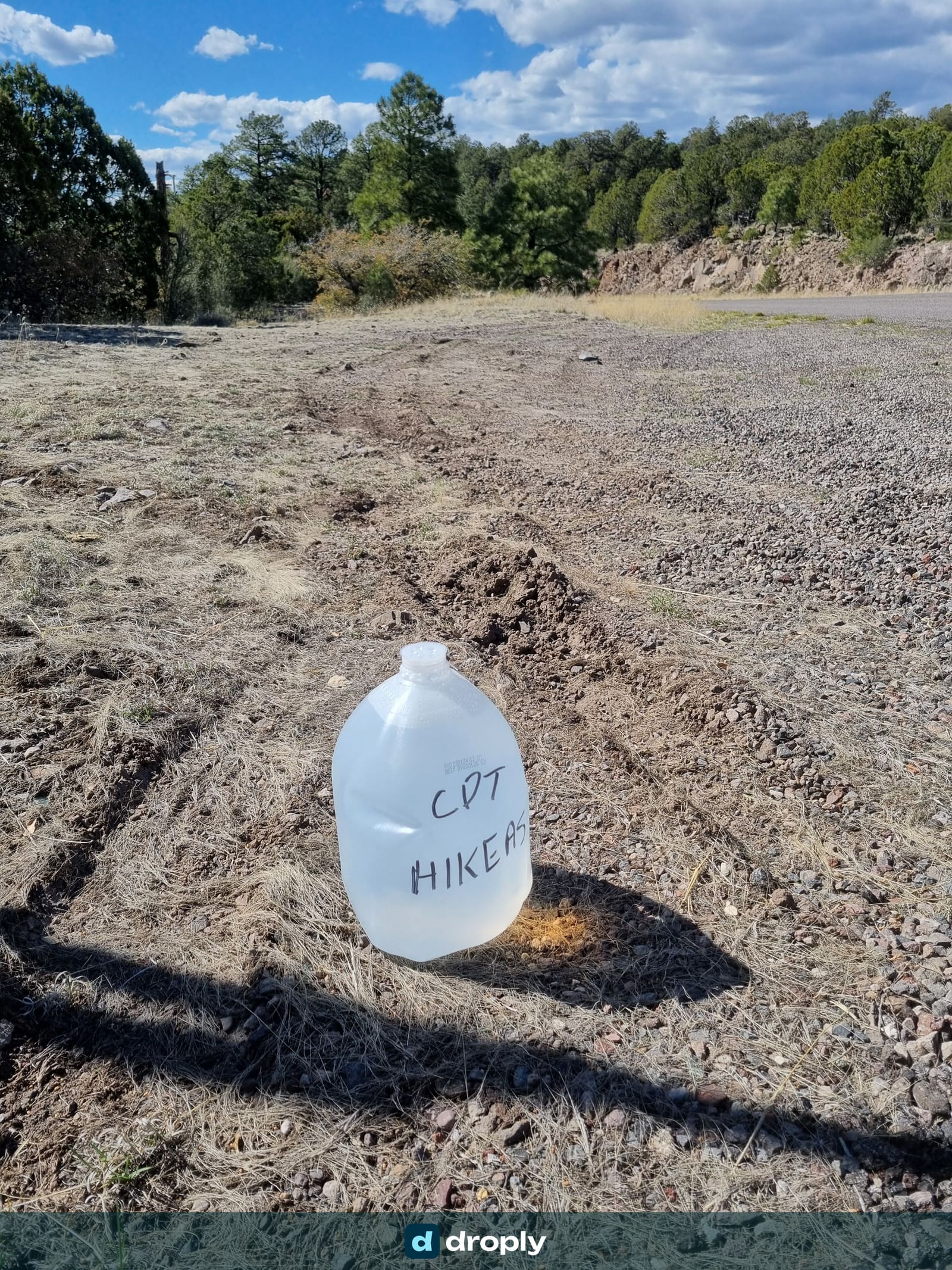 A plastic gallon jug labelled 'CDT Hikers' left on a gravel road