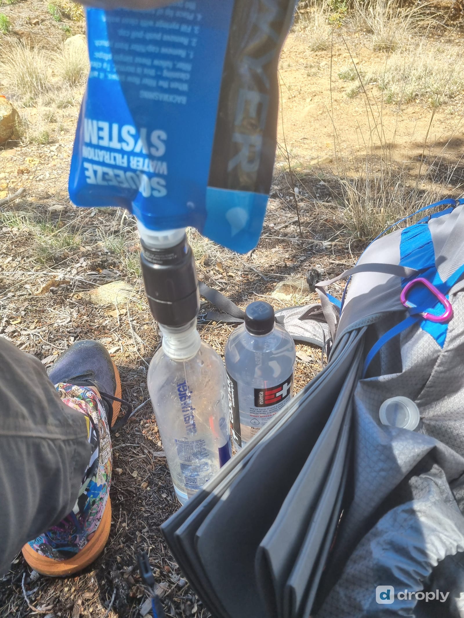 Sawyer Squeeze filter in use on trail, filtering water directly into a reused plastic bottle
