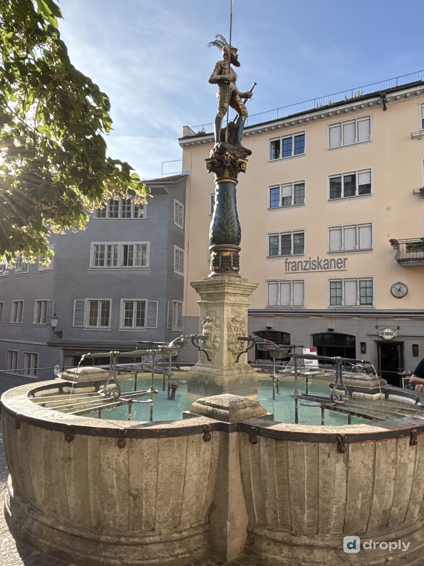 The Stüssibrunnen with a gilded figure and shimmering blue water in Zurich's old town