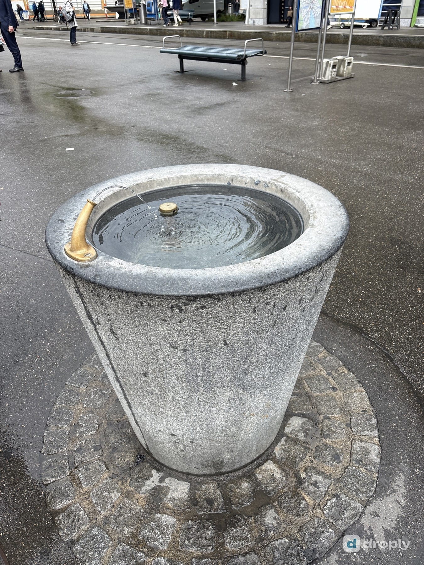 A simple stone drinking fountain with a golden spout at Paradeplatz in Zurich