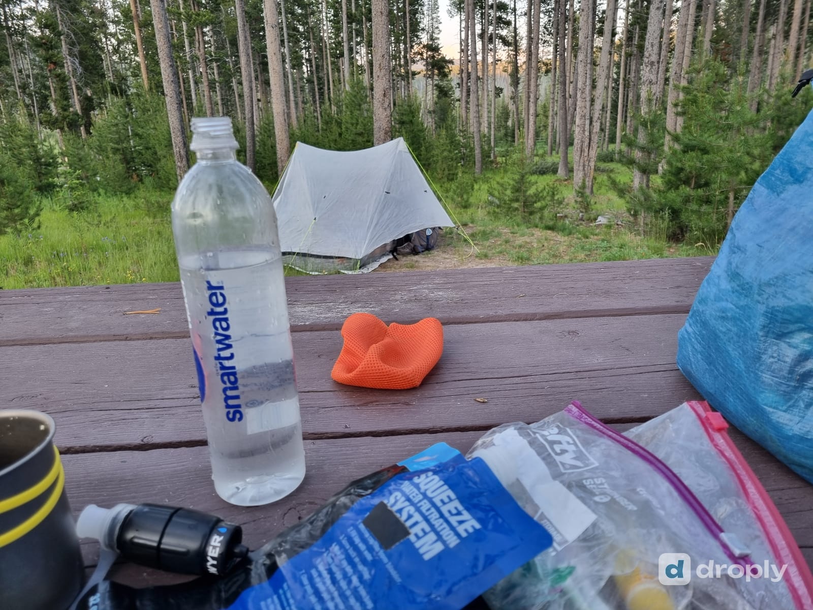 A squeeze filter system and a bottle of filtered water at a forest campsite, tent visible in the background