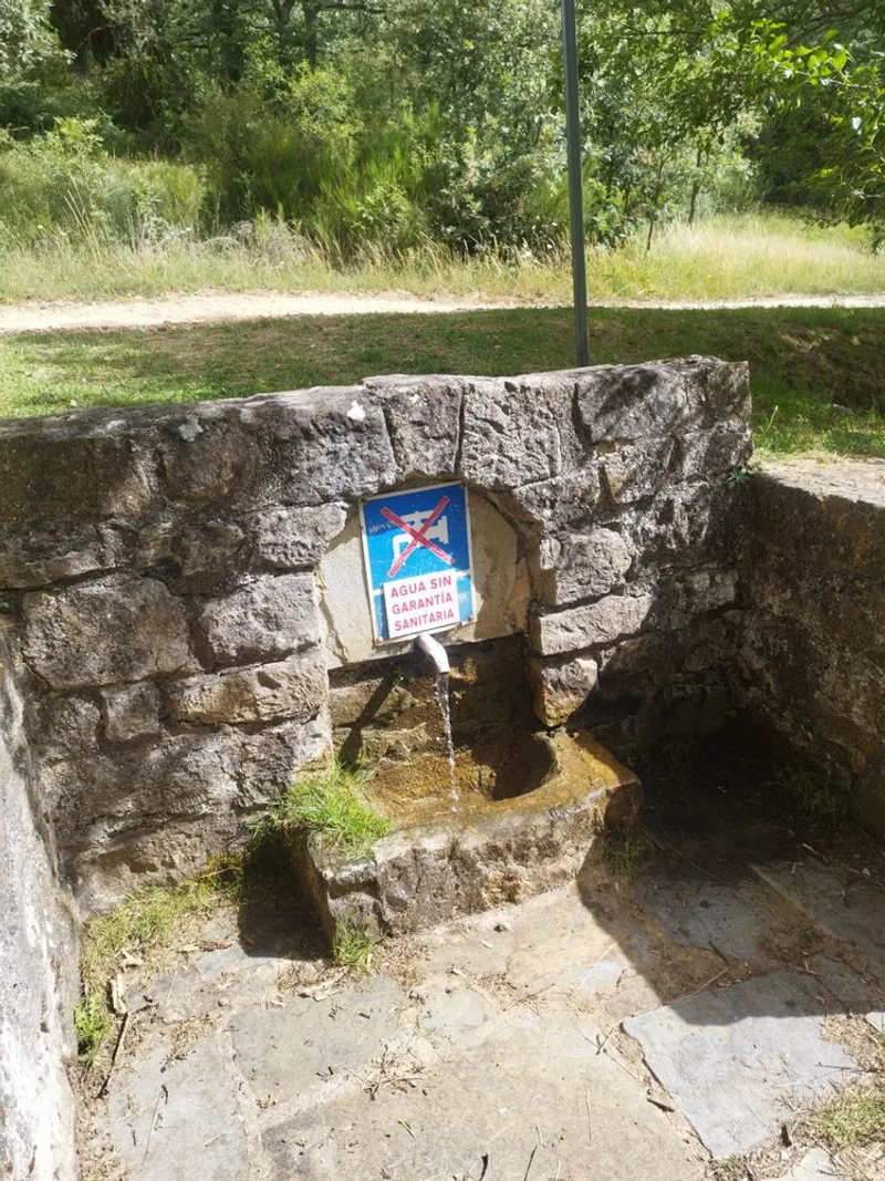 A stone fountain along the Camino de Santiago in La Rioja, Spain, its agua sin garantía sanitaria sign a reminder that…